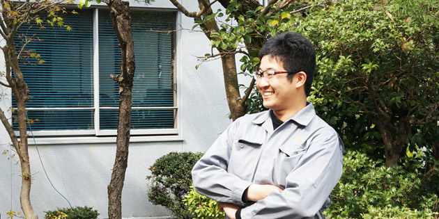 浪速精密工業の作業着を着て屋外で腕を組む光井隆介さん