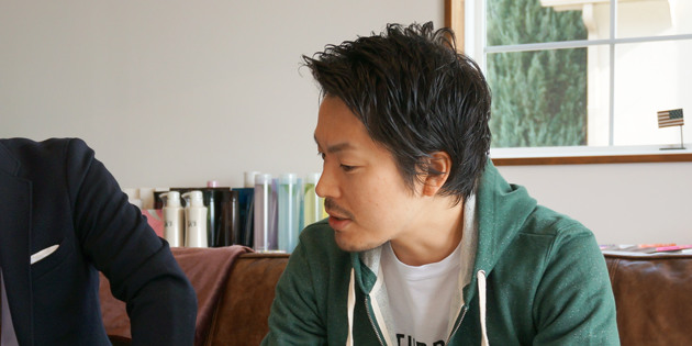 緑色のパーカーを着てソファに座り笑顔で話す西田誠さん