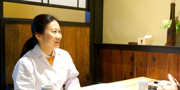 調理服を着てテーブル席で身振りを交えて話す大前輝伽子さん