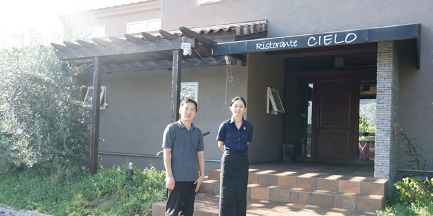 リストランテ シエロの坂東友也さんと坂東右子さんが店の外観の前に立っている様子