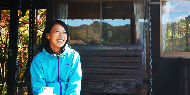 青いジャケットを着た大林由佳さんが屋外の椅子に座り笑顔で話している様子