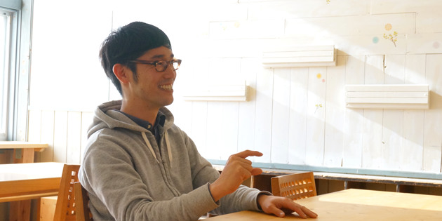 井上達哉さんがテーブルで指を差しながら笑顔で話している様子