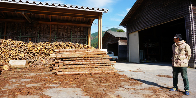 村楽エナジーの井筒耕平さんが薪の保管場所の前に立っている様子