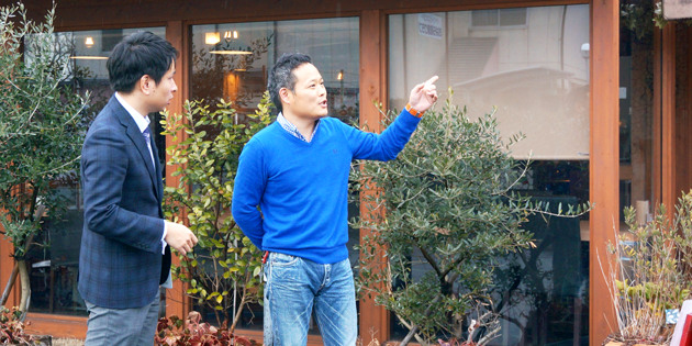 店舗の前で指を差して方向を示している寄木秋弘さん