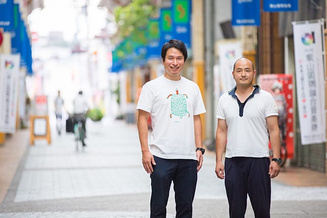 商店街に立つ北村暢宏氏とインタビュアー