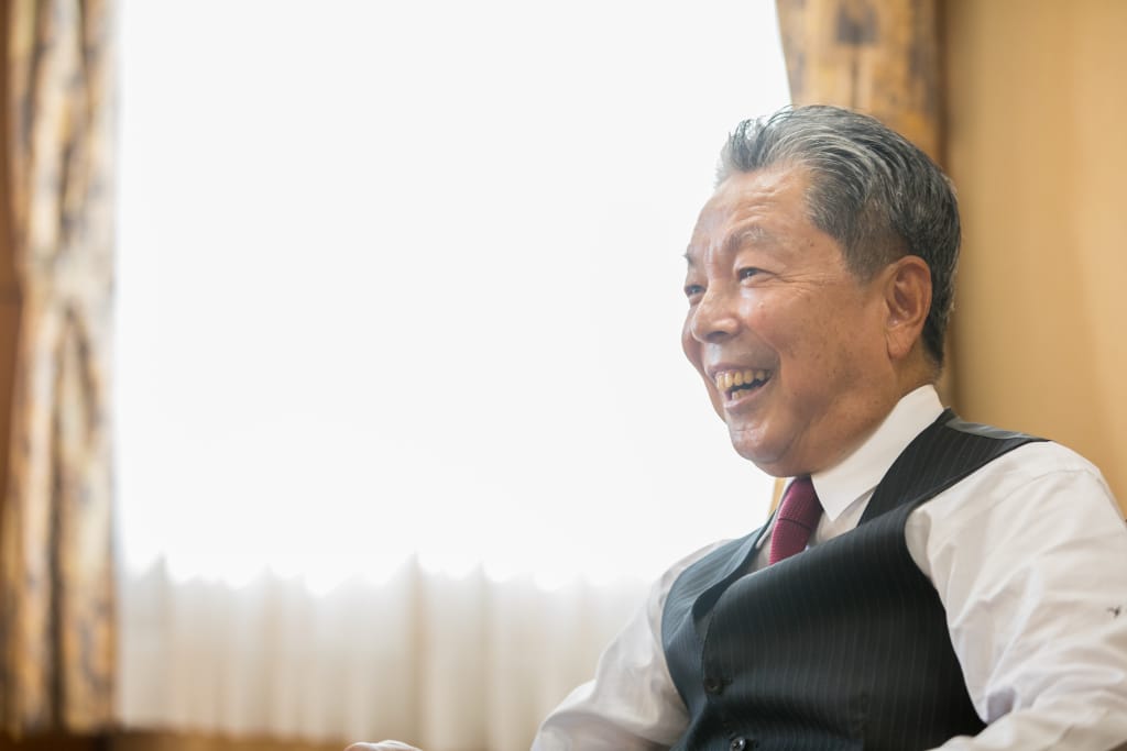 笑顔でインタビューに答える浮田芳典理事長の横顔。