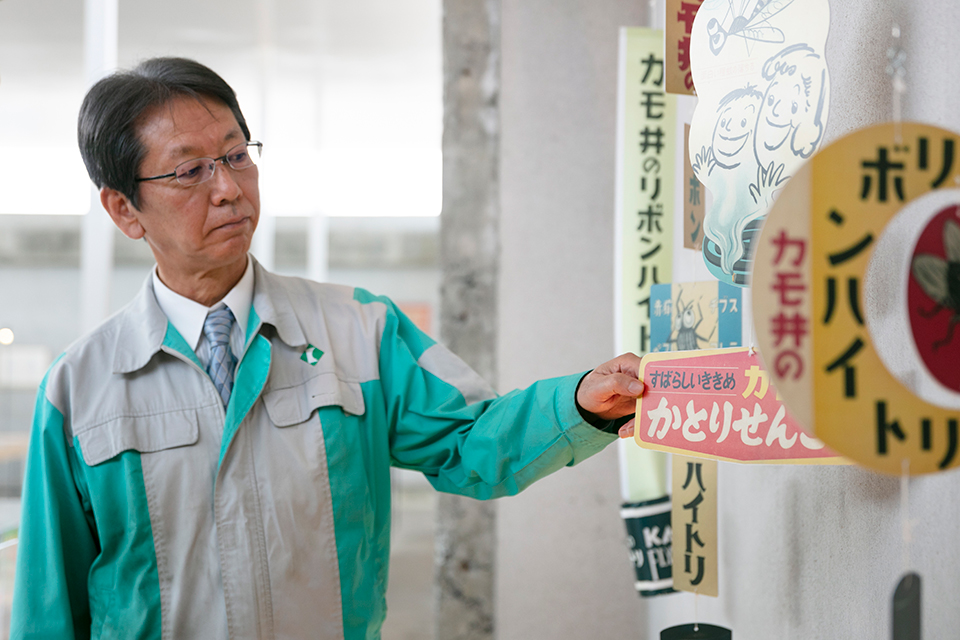 展示されている「カモ井のリボンハイトリ」を指し、その歴史について説明する鴨井社長。