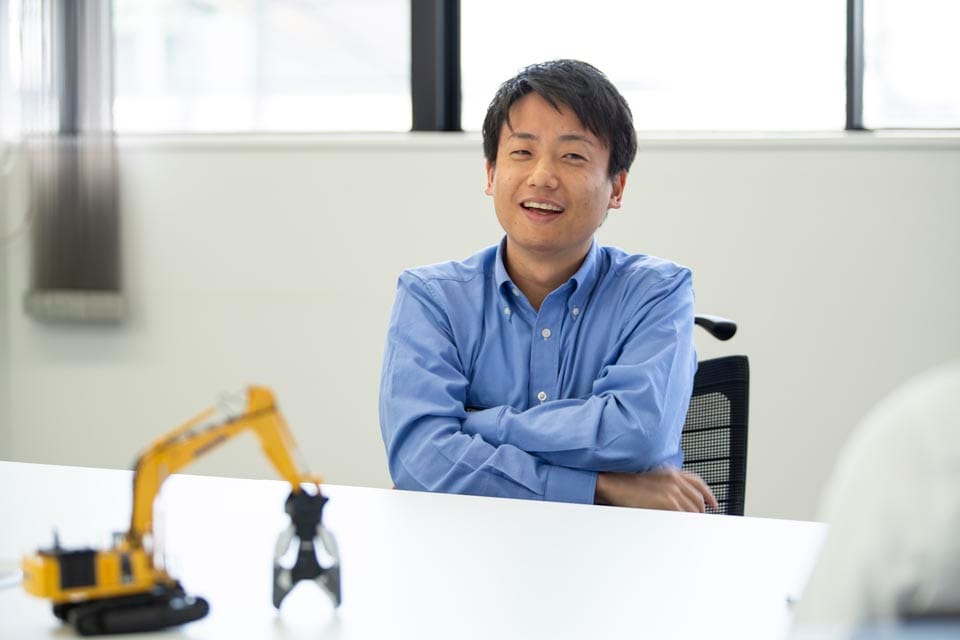 腕を組んで微笑みながらインタビューに答える田口博章氏。