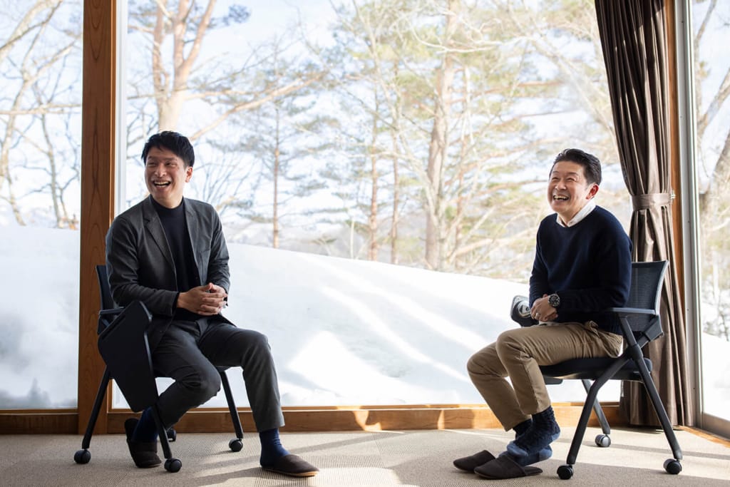 雪景色の見える大きな窓を背景に、院庄林業の武本哲郎氏（右）とインタビュアー（左）が椅子に座って対談している。
