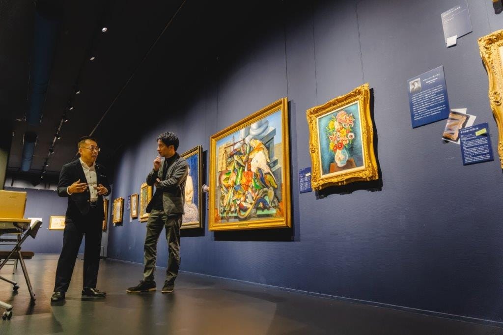 アートギャラリーの絵画の前で、インタビュアーに説明をする山田英生社長