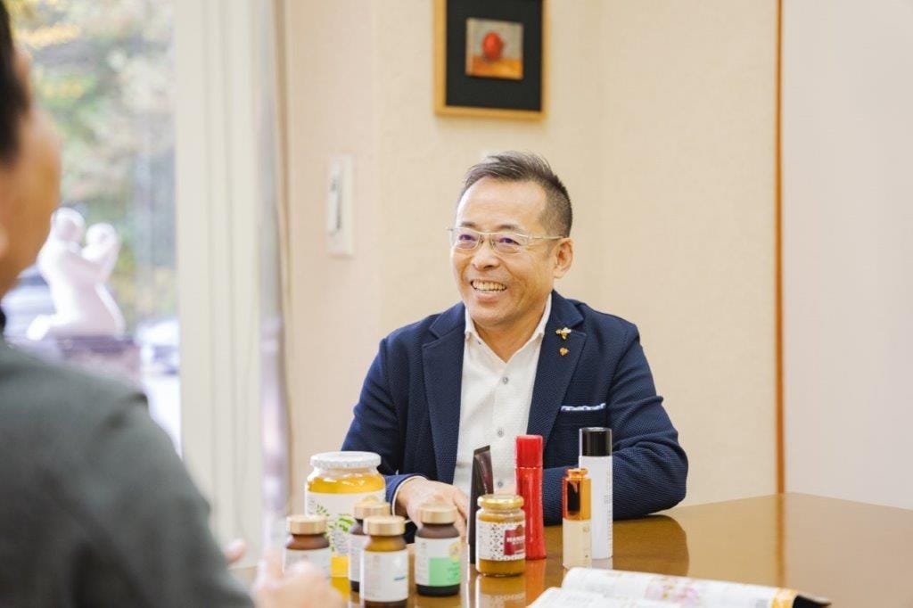 応接室のテーブルで、商品を前に笑顔でインタビューに答える山田英生社長。