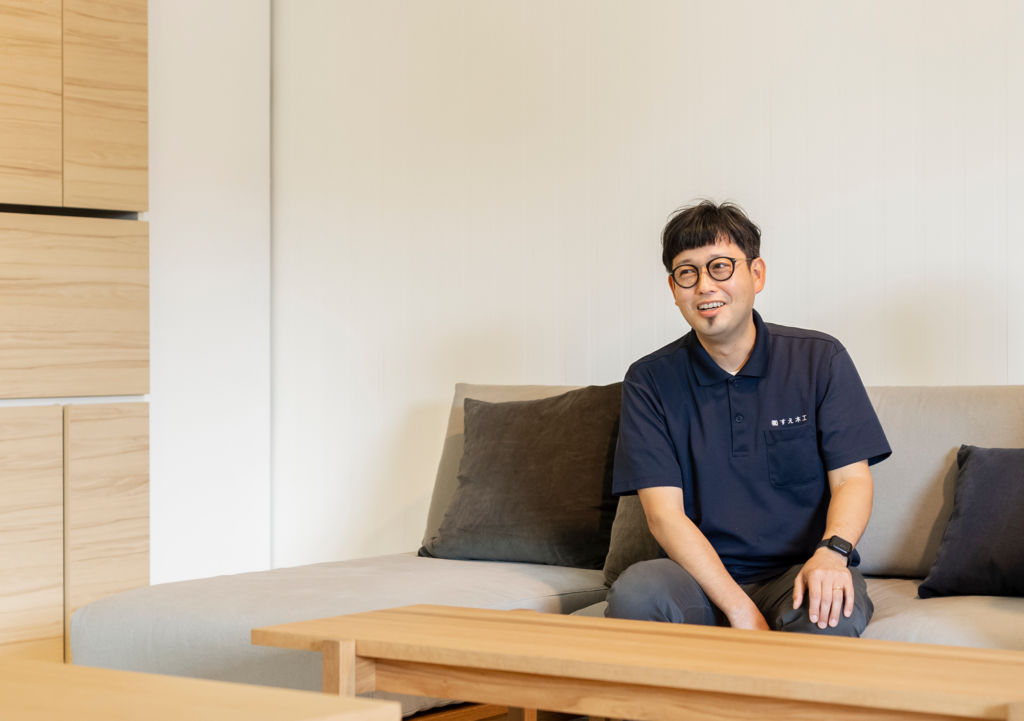 ソファに座りインタビューに答える、株式会社すえ木工の須江健治社長。