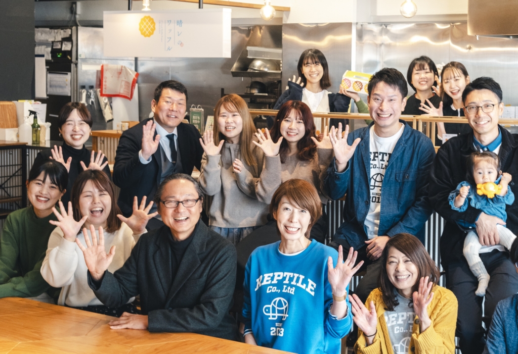 ワッフル店の店内でカメラに向かって手を振るスタッフたちの集合写真
