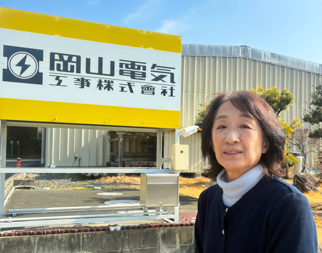 会社の看板と、その前に立つ市村浩子さん