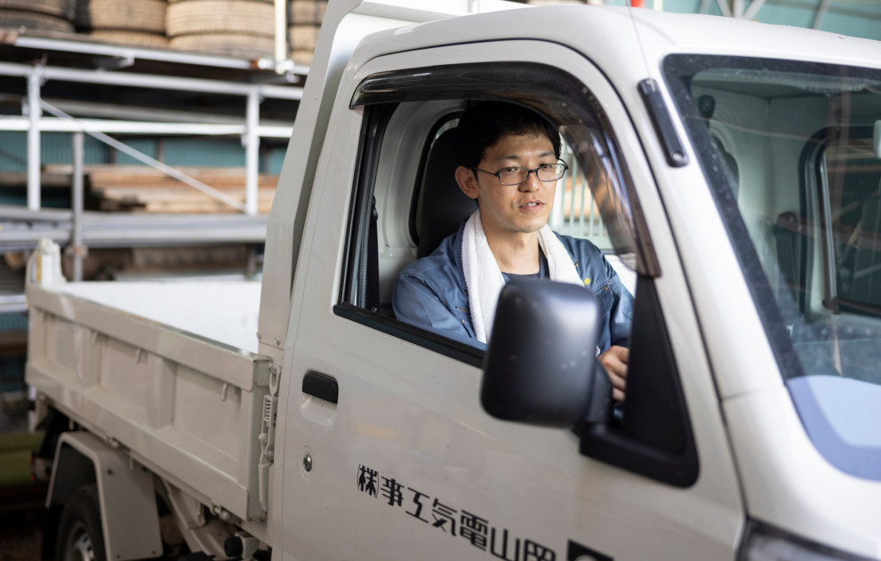 社用車の軽トラックを運転する作業着姿の男性社員