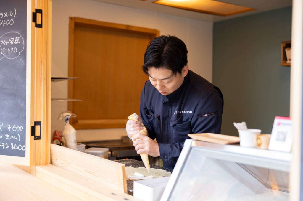 「KIKORU」のカウンター内で、うじひら木材産業の氏平雄人代表取締役がクレープにホイップクリームを盛り付けている。