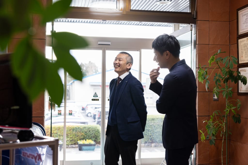 共和機械の玄関で、インタビュアーと笑顔で話す友末琢磨社長。