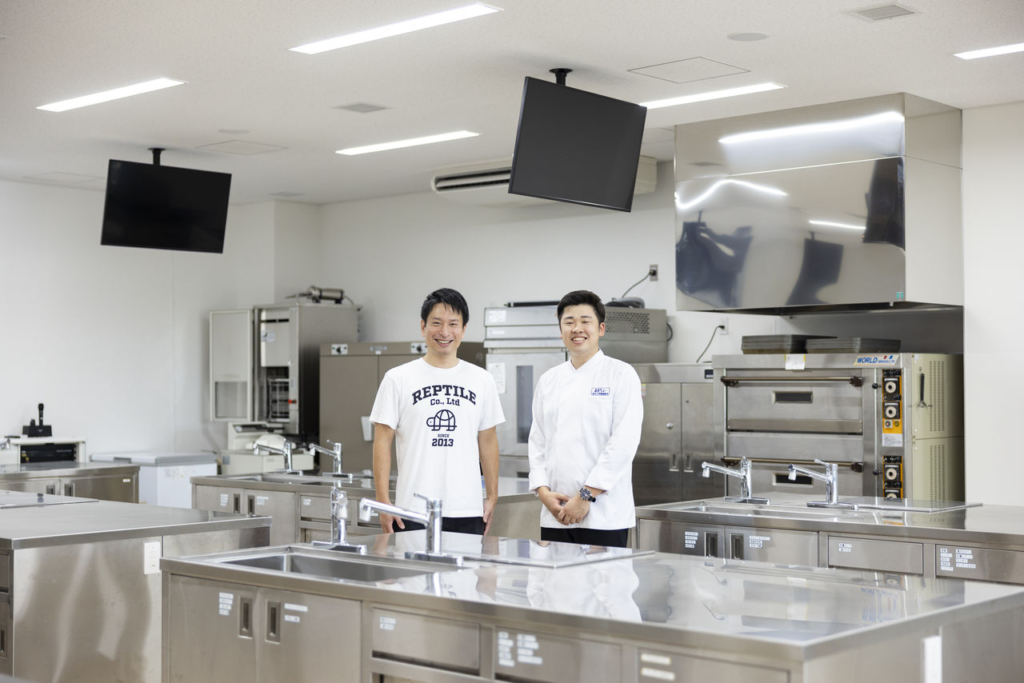 美作大学の調理室で、インタビュアーと並んで記念撮影に応じる牧原直太朗さん。