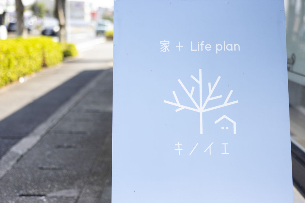 屋外に設置された、空色の背景に白の単色でロゴが描かれているフラットなデザインの看板。