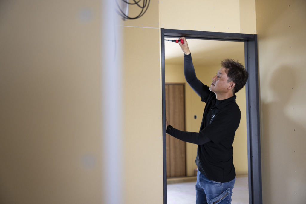 住宅の室内で、キノイエの男性スタッフがドア枠の調整作業を行っている。