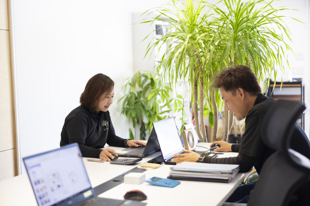 株式会社キノイエのオフィス内で、男女2名のスタッフが並んでデスクに座り、それぞれのノートパソコンで業務を行っている。