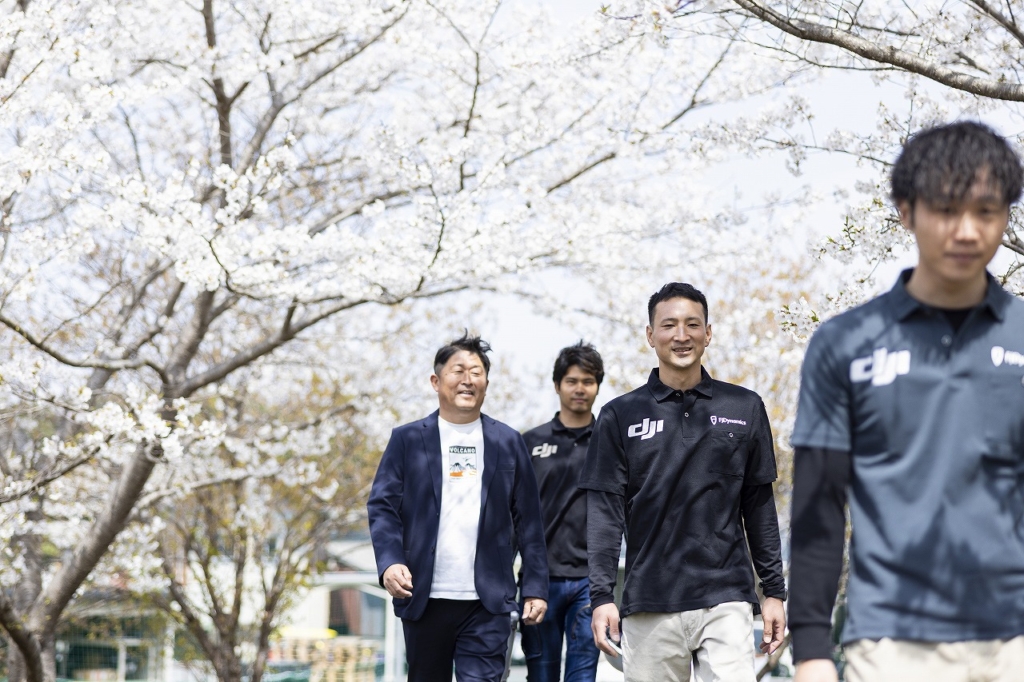 桜の木の下を歩く社員4名