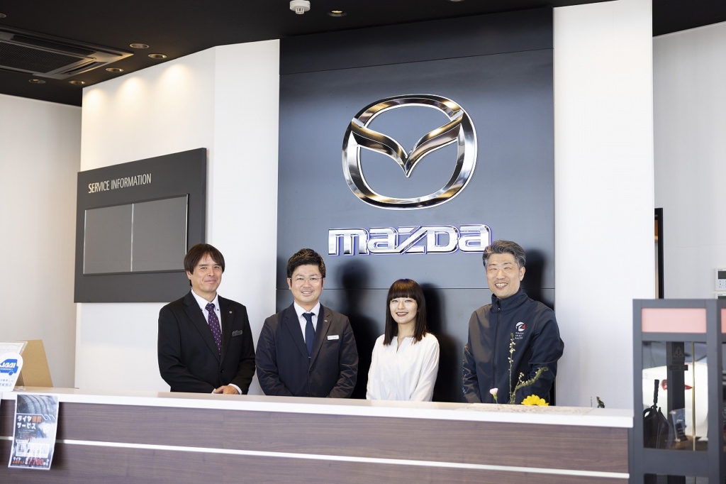 マツダのロゴの前で笑顔の集合写真を撮影する社員達