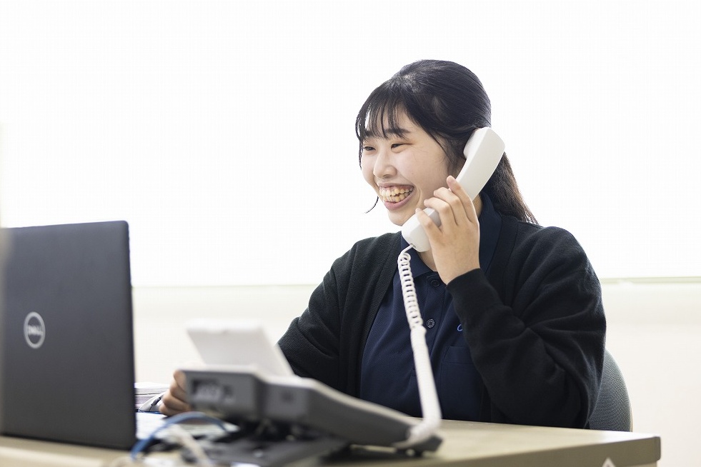 尼﨑工作所岡山工場の総務スタッフ。笑顔で電話を受ける様子。