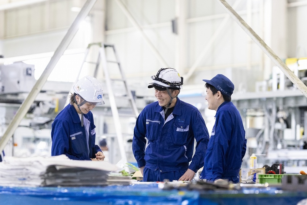 尼﨑工作所の工場で笑顔で議論する3名のエンジニア、活発な意見交換とチームワーク