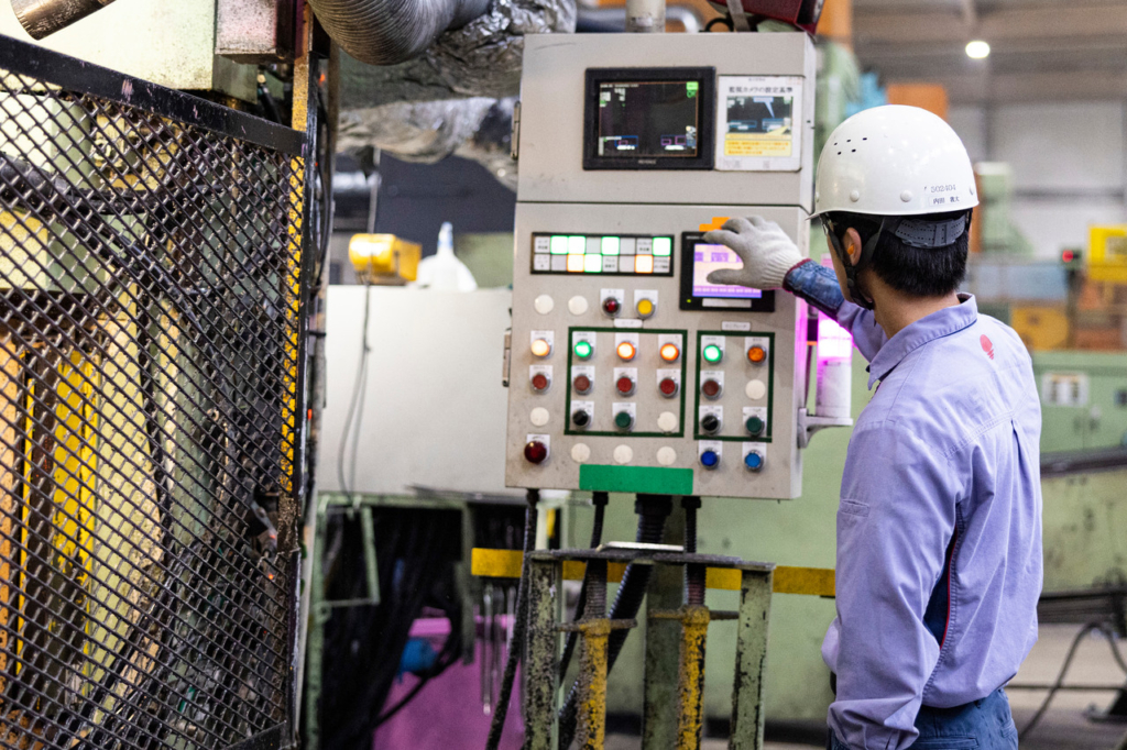 工場内でヘルメットを着用した男性社員が機械の操作パネルをタッチしている様子