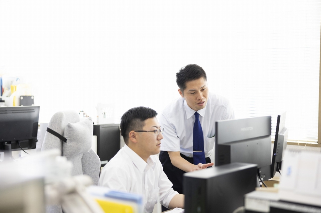 オフィスで、2人の男性従業員がコンピューター画面を一緒に見ながら議論している様子