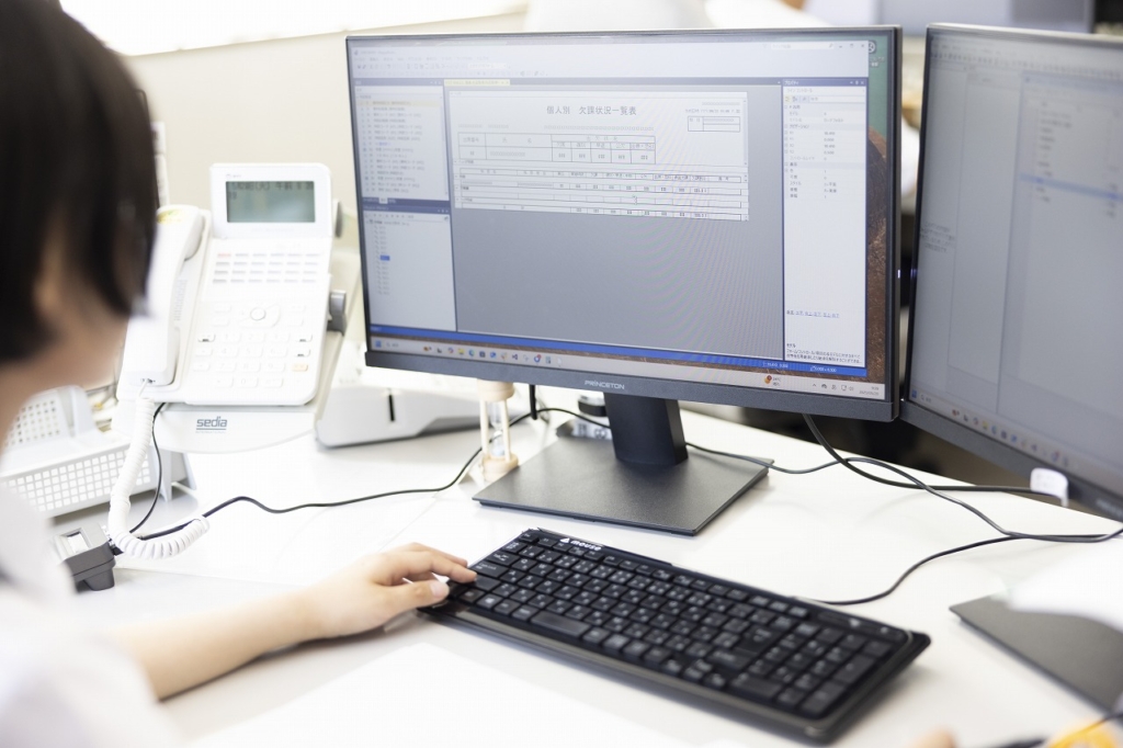 オフィスデスクでコンピューターのキーボードを操作しており、画面にはデータやリストが表示されている様子