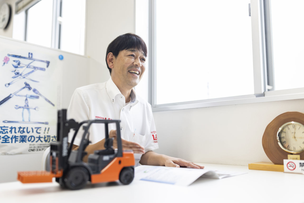 トヨタL&F岡山 津山営業所の北畠所長。デスクに置かれたフォークリフトのミニチュアを前に、笑顔でインタビューに答える。