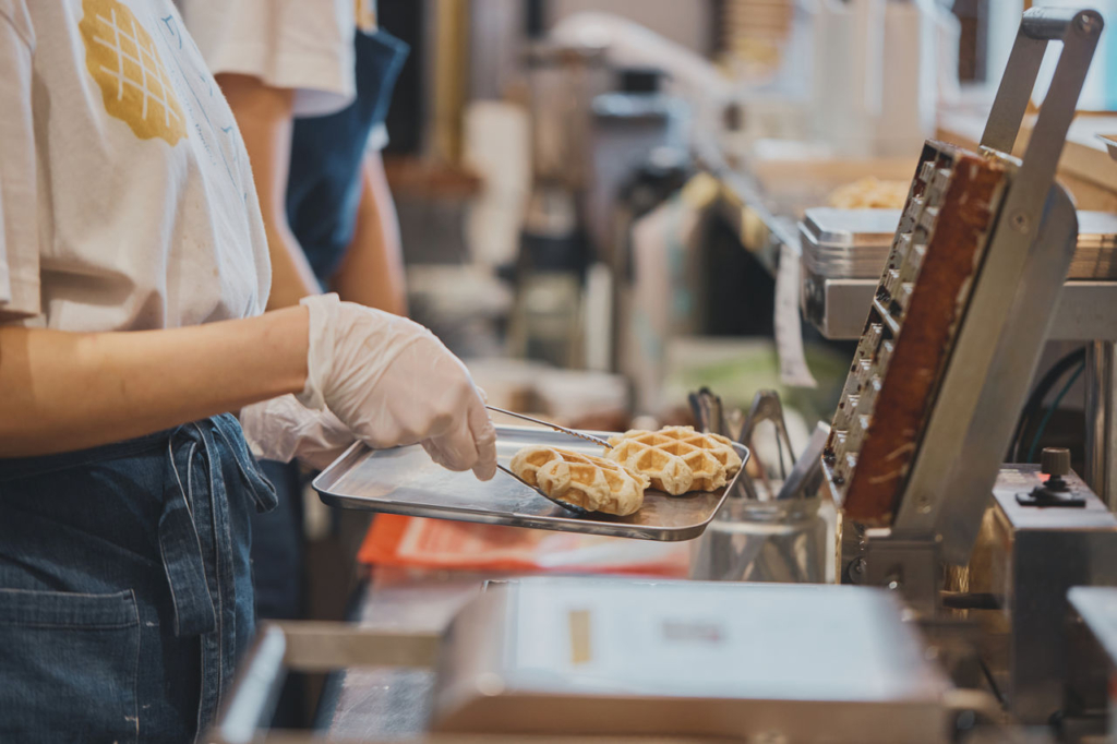 スタッフが業務用ワッフルメーカーで焼きあがったワッフルをトングで取り出している様子。