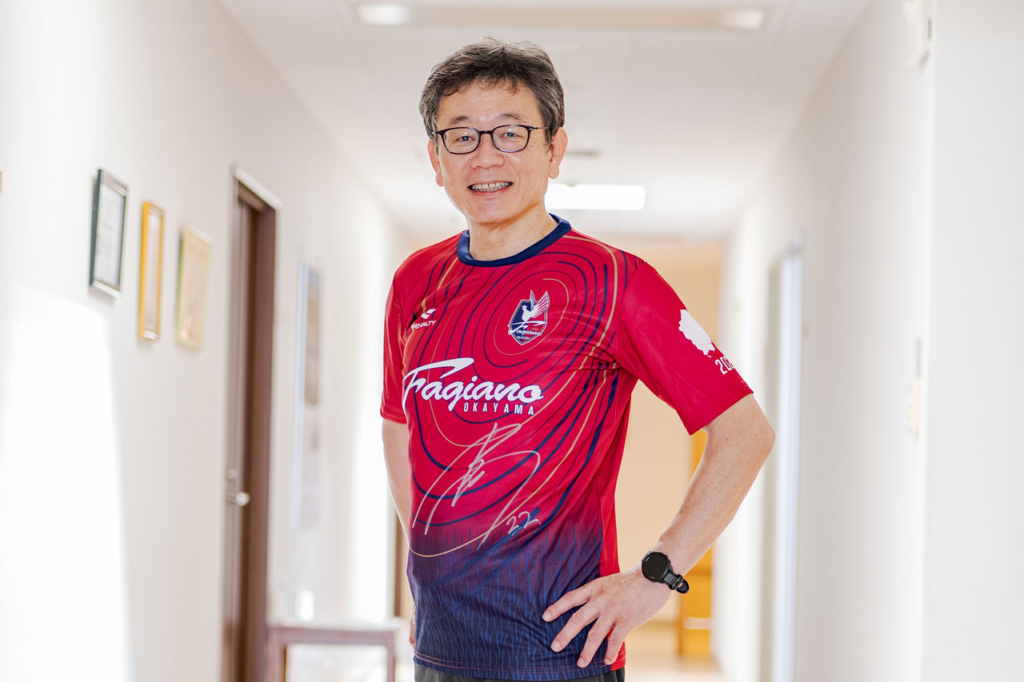 サッカーチームのユニフォームを着た津山中央病院の岡岳文病院長が腰に手を当てて立っている。