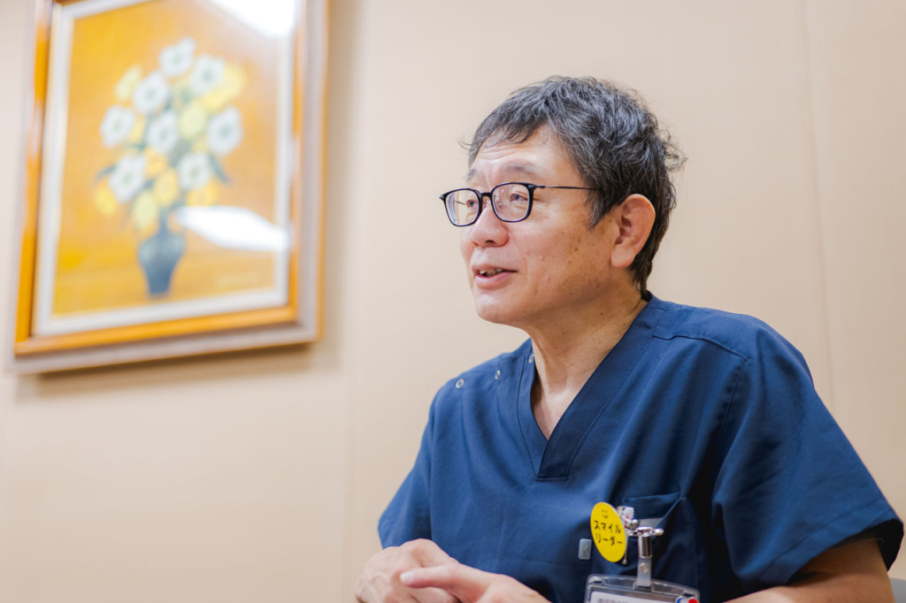 津山中央病院の病院長、岡岳文医師が紺色のスクラブ姿で話している。