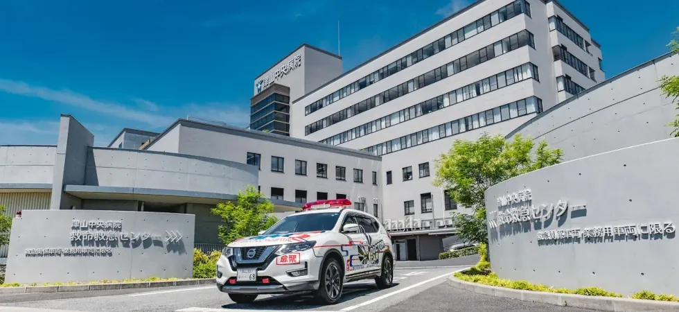 津山中央病院の建物と、救命救急センターの看板の前に停車しているドクターカー。