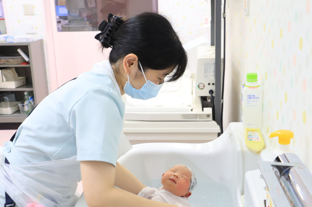 助産師がベビーバスで新生児を沐浴させている。