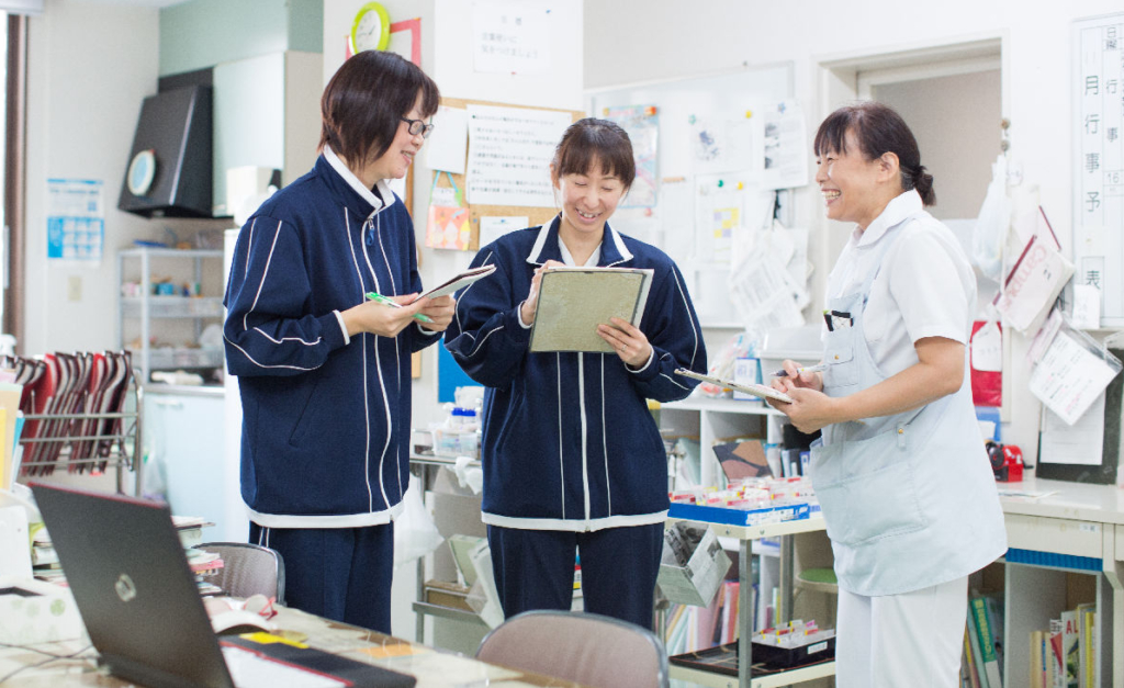 オフィス内で3人の女性スタッフがタブレットや書類を見ながら話している。