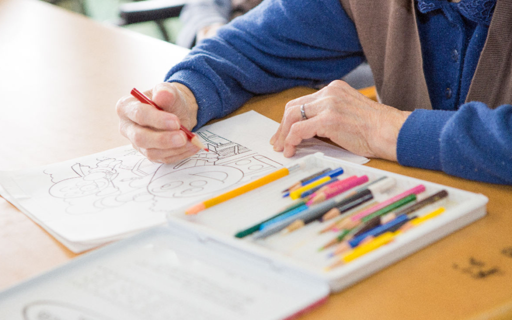 高齢の利用者がテーブルで色鉛筆を使い、塗り絵をしている手元。