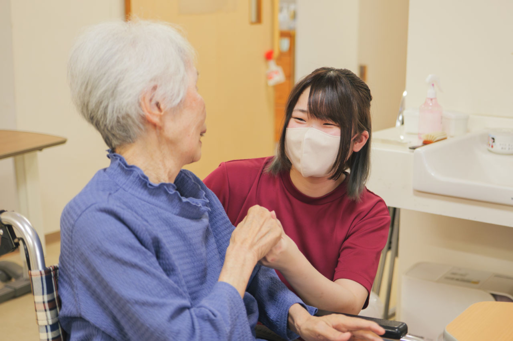 若い女性介護士が車椅子の利用者に寄り添って話している様子