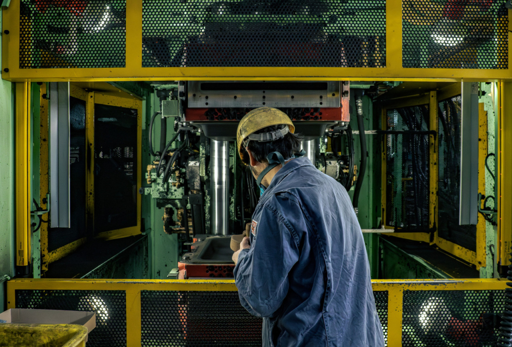 緑色の大型自動造形機の前に立ち、操作パネルを扱う作業員