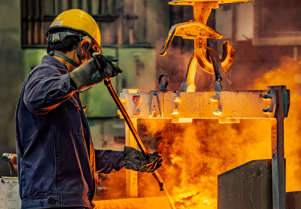 工場内でクレーンで吊られた取鍋から溶けた金属を注ぐ作業