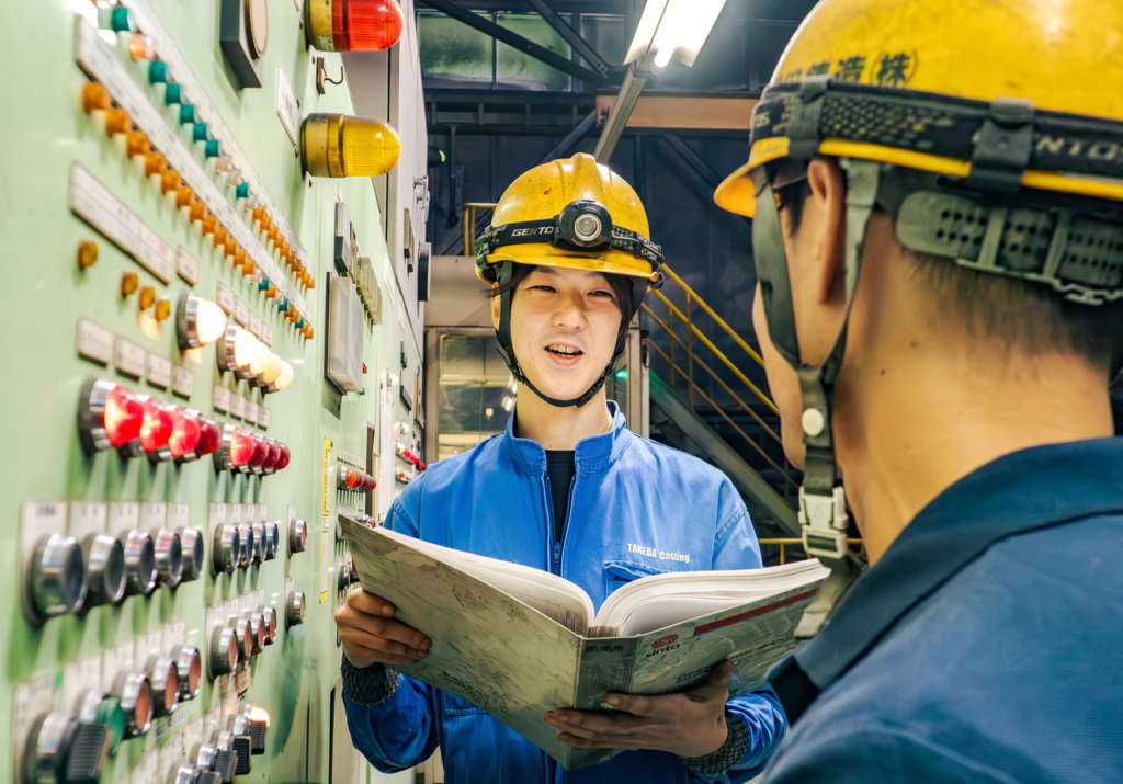 マニュアルを片手に持ち、機械の操作パネルを確認している男性作業員