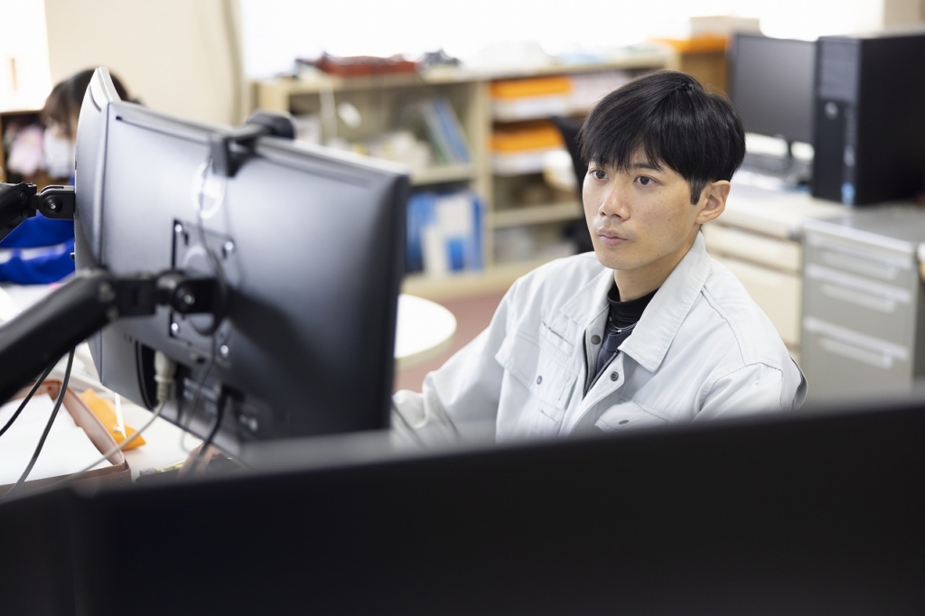 オフィスでモニターを見つめ、PC作業を行っている男性社員