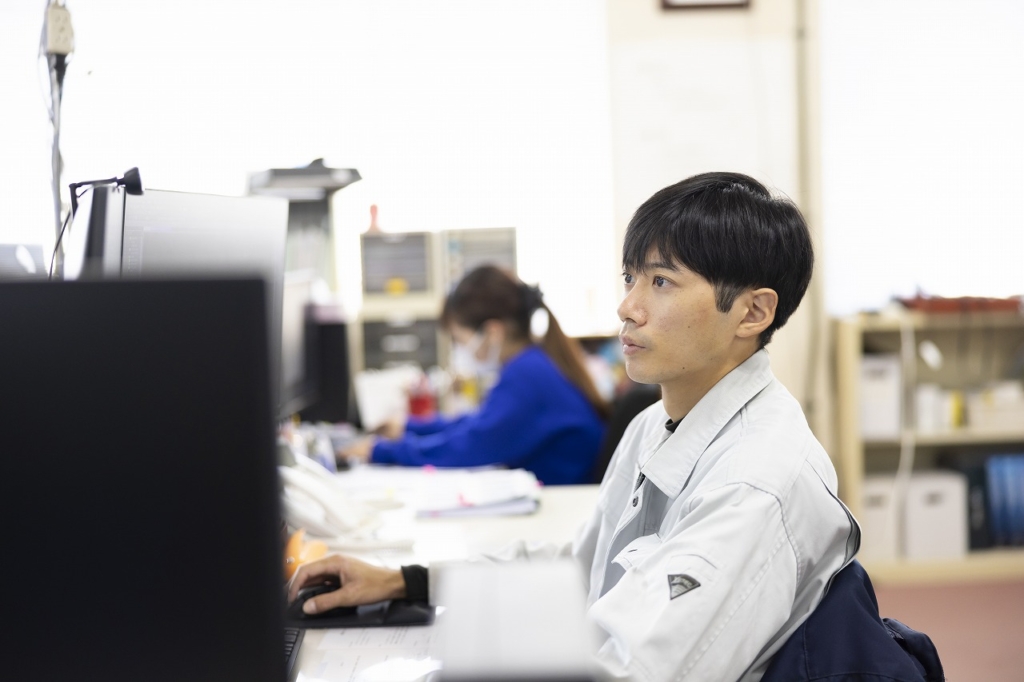 デスクでPCモニターを見つめ、業務を行う大坪さん