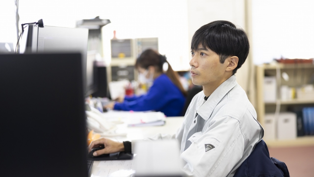 デスクでPCモニターを見つめ、業務を行う大坪さん