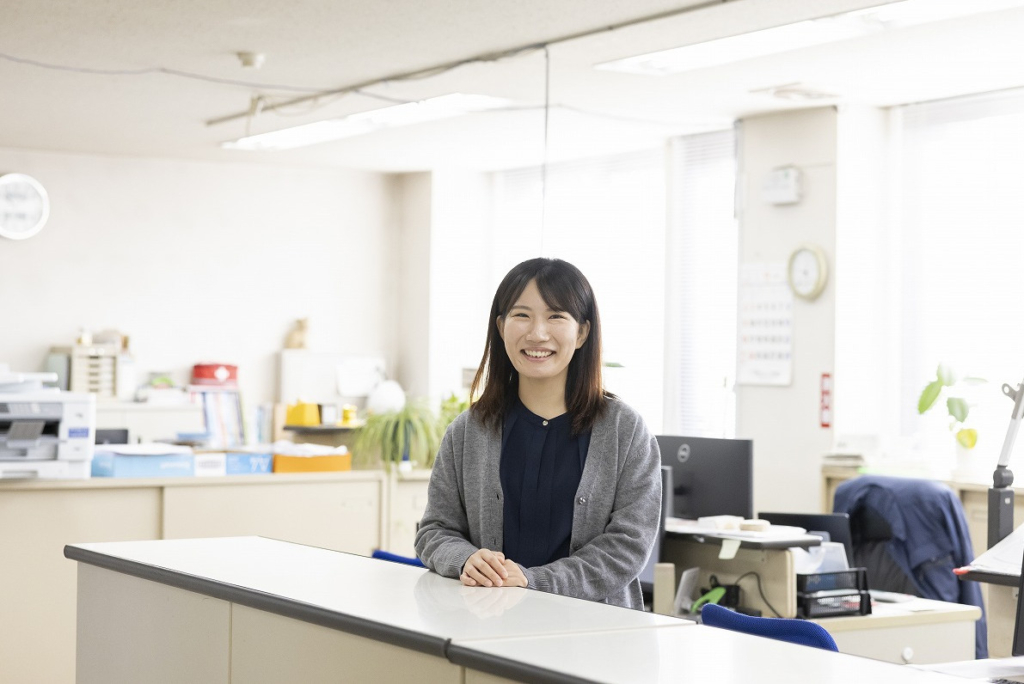 受付カウンターに手を置き、笑顔で立つ女性社員