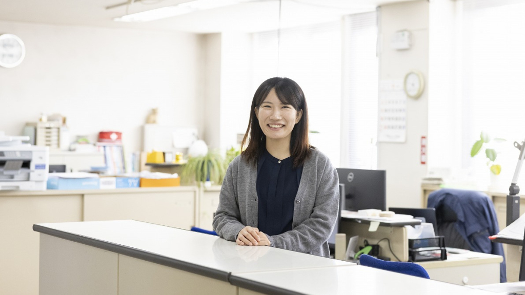 受付カウンターに手を置き、笑顔で立つ女性社員