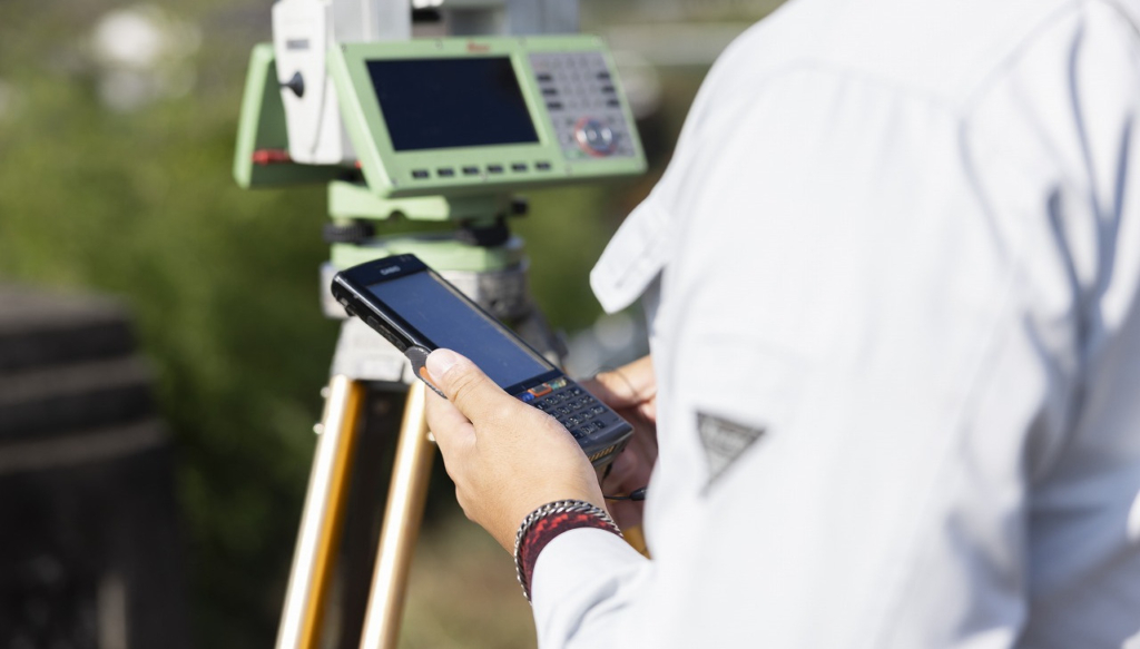 三脚に固定された機器の前でデータコレクタを操作する手元